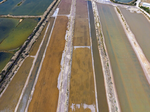 Aerial view of geometric salt pans with varying water levels and earthy tones in Moncarapacho, Faro District, Portugal.