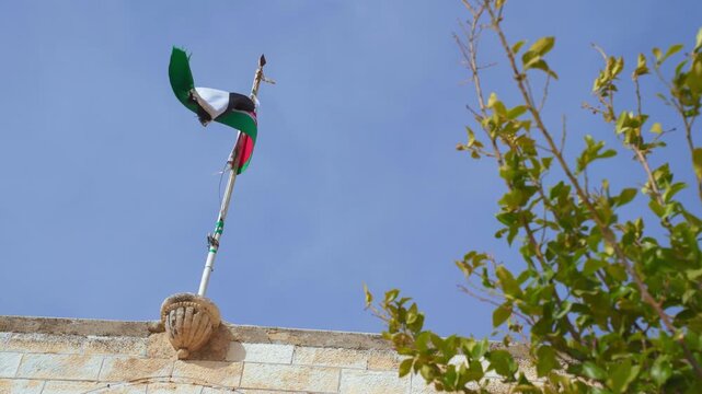 Jordan flag, torn little bit at edge, on a pole at top of building waving in a wind