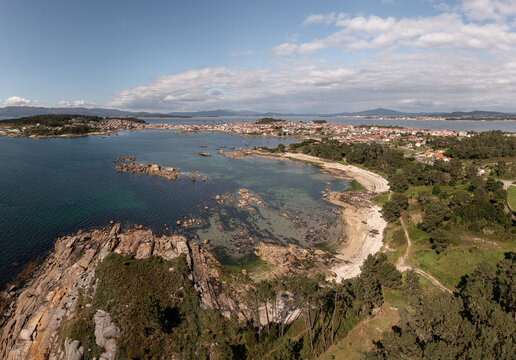 Aerial view of the coastal town of A Illa de Arousa with its rocky shoreline, sandy beach, and surrounding greenery in A Illa de Arousa, Pontevedra, Spain.