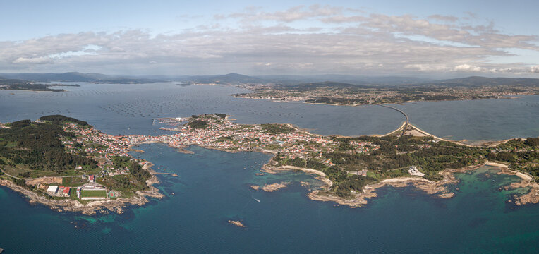 Aerial view of A Illa de Arousa town with its bridge, rocky coastline, and mussel rafts in the bay of A Illa de Arousa, Pontevedra, Spain.