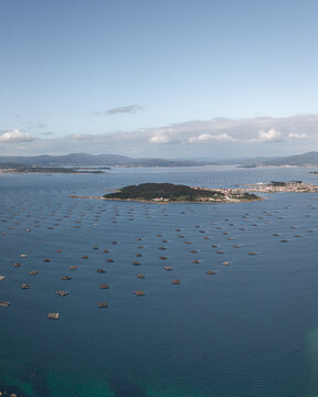Aerial view of A Illa de Arousa surrounded by numerous mussel rafts in the blue waters of the Rias Baixas, with distant hills in A Illa de Arousa, Pontevedra, Spain.
