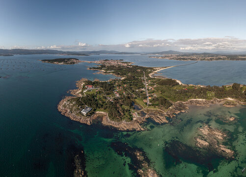 Aerial view of the coastal landscape of A Illa de Arousa with turquoise waters, rocky shoreline, lush greenery, and the bridge connecting to the mainland in A Illa de Arousa, Pontevedra, Spain.