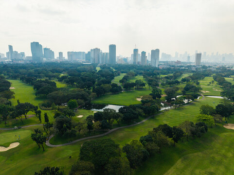 Aerial view of Wack Wack Golf Country Club with lush green fairways, trees, and a pond, set against the modern skyline of Manila, Metro Manila, Philippines.