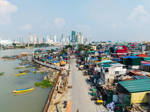 Aerial view of Barangay 649 along the Pasig River with small wooden boats, dense urban housing, and the modern city skyline in the background in Manila, Metro Manila, Philippines.