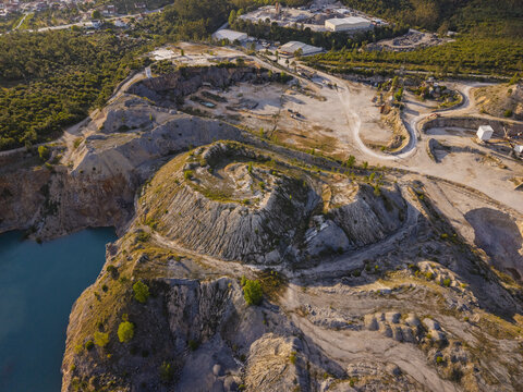 Aerial view of Miradouro da Pedreira Azul featuring a striking turquoise quarry lake surrounded by rugged rocky terrain and a spiral path in Redinha, Leiria, Portugal.