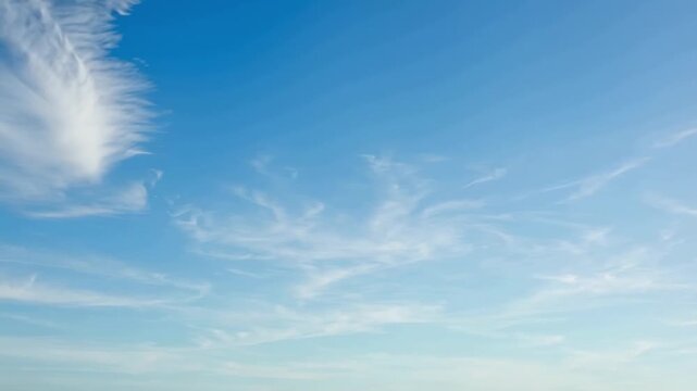 Slow pan of wispy cirrus clouds drifting across wide blue sky above horizon during calm clear morning. subtle cloud motion reveals changing light and textures