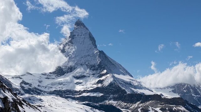 Aerial view of the iconic Matterhorn mountain peak with snow-covered slopes and clouds under a clear blue sky in Zermatt, Valais, Switzerland.