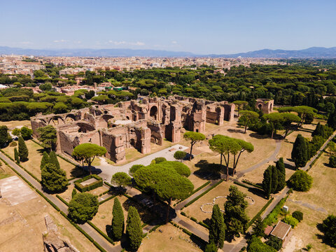 Aerial view of the ancient Roman ruins of the Baths of Caracalla surrounded by lush pine trees and parkland with the city skyline of Rome in the background, Roma, Lazio, Italy.