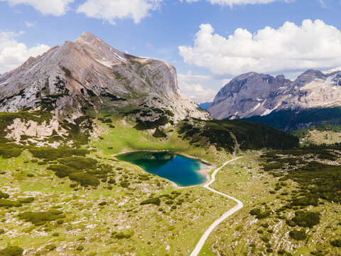 Aerial view of Lago Limo surrounded by lush green meadows and rugged mountain peaks in the Dolomites near Marebbe, Trentino-Alto Adige, Italy.