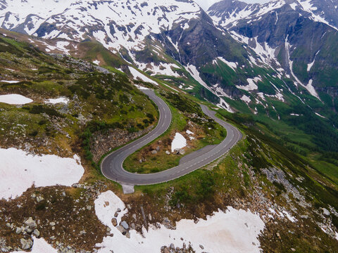 Aerial view of the winding Grossglockner High Alpine Road surrounded by snow-capped mountains and green slopes in Zell am See District, Salzburg, Austria.