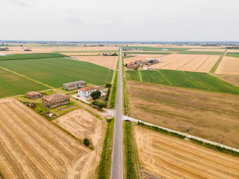 Aerial view of Via Imperiale road cutting through vast agricultural fields with farmhouses and cultivated land in Ferrara, Emilia-Romagna, Italy.