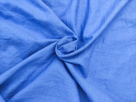 Top view of bright blue wrinkled fabric texture background with elegant swirl folds.