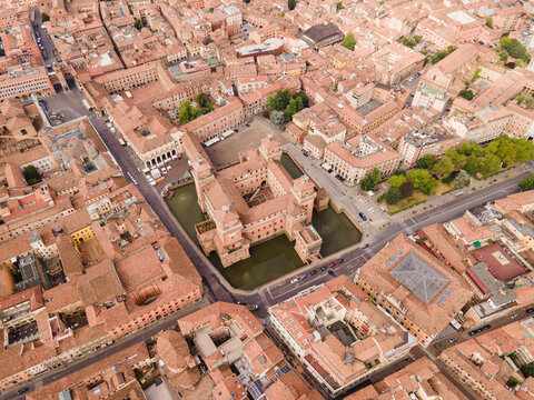Aerial view of Estense Castle surrounded by a moat and historic terracotta rooftops in the city center of Ferrara, Emilia-Romagna, Italy.