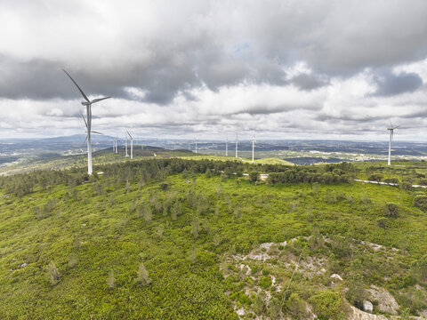 Aerial view of Parque Eolico da Serra dos Candeeiros with wind turbines on a green rolling hillside under a cloudy sky Rio Maior, Santarem, Portugal.