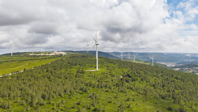 Aerial view of Parque Eolico da Serra dos Candeeiros featuring wind turbines set against a lush green hilly landscape under a cloudy sky in Rio Maior, Santarem, Portugal.