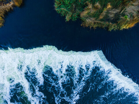 Aerial view of Venta Rapid, the widest waterfall in Europe, with white foaming water cascading over the rocky ledge into the dark river in Kuldiga, Kuldiga Municipality, Latvia.