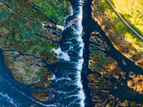 Aerial view of Venta Rapid, the widest waterfall in Europe, showing the flowing water, rocky riverbed, and lush green banks in Kuldiga, Kuldiga Municipality, Latvia.