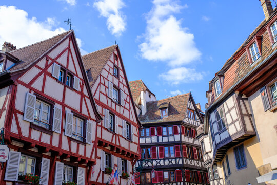 France - 09 July 2026: View of traditional half-timbered houses with red shutters and steep roofs under a clear blue sky in an Alsatian village.