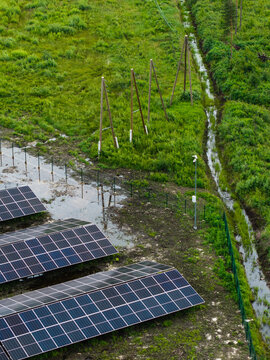 Aerial view of solar panels installed in a grassy field near a small stream and wooden utility poles in Suntazi, Ogre Municipality, Latvia.