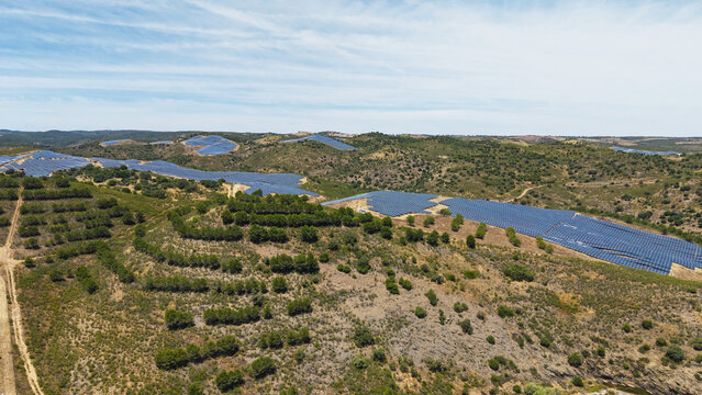 Aerial view of a large solar farm with rows of photovoltaic panels installed across the rolling hills of the countryside in Vaqueiros, Faro District, Portugal.