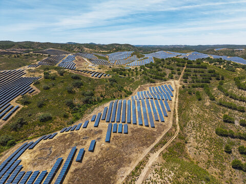 Aerial view of a large solar farm with rows of photovoltaic panels installed on rolling hills in the countryside of Vaqueiros, Faro District, Portugal.