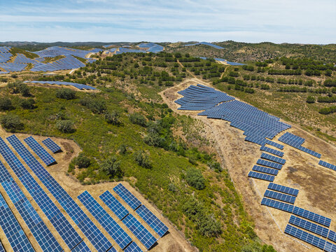 Aerial view of a large solar farm with rows of photovoltaic panels installed on rolling hills in the rural landscape of Vaqueiros, Faro District, Portugal.