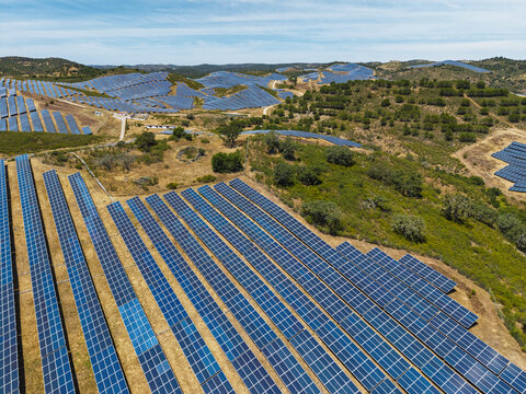 Aerial view of a large solar farm with rows of photovoltaic panels installed across rolling hills in the rural landscape of Vaqueiros, Faro District, Portugal.