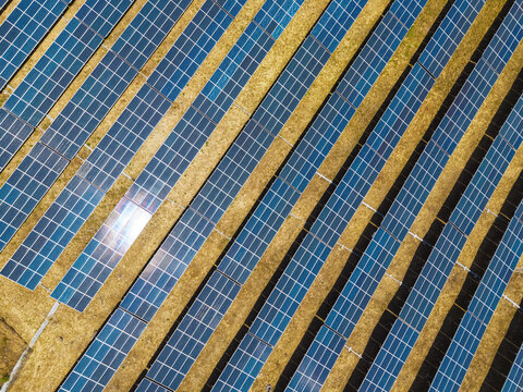 Aerial view of rows of solar panels installed on dry golden fields in a solar farm in Vaqueiros, Faro District, Portugal.