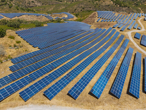 Aerial view of a large solar farm with rows of photovoltaic panels installed on dry, hilly terrain in Vaqueiros, Faro District, Portugal.
