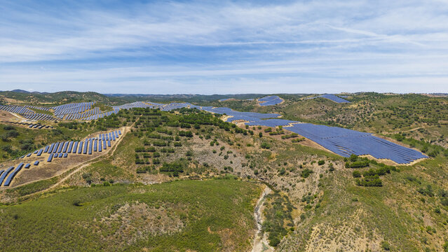 Aerial view of a large solar farm with rows of photovoltaic panels installed across the rolling green hills of the countryside in Vaqueiros, Faro District, Portugal.