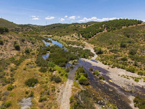 Aerial view of a winding river flowing through the rural landscape, surrounded by rolling hills and Mediterranean vegetation in Vaqueiros, Faro District, Portugal.