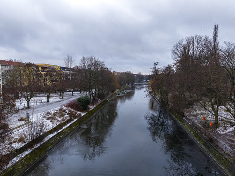 Aerial view of the Landwehr Canal in Friedrichshain-Kreuzberg, featuring snow-covered banks, bare winter trees, and calm water under a cloudy sky in Berlin, Berlin, Germany.