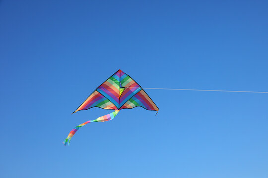 Colorful rainbow delta kite flying high in clear blue sky