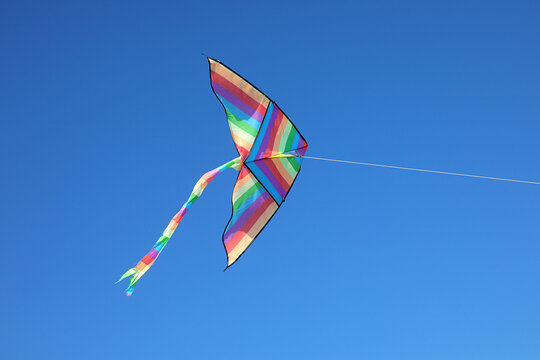 Colorful rainbow kite flying high in clear blue sky
