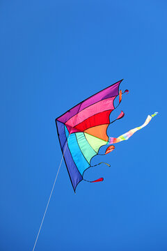Colorful rainbow kite flying high in clear blue sky