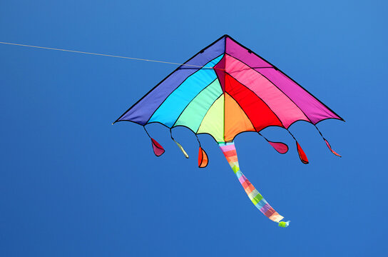 Colorful rainbow kite flying high in clear blue sky