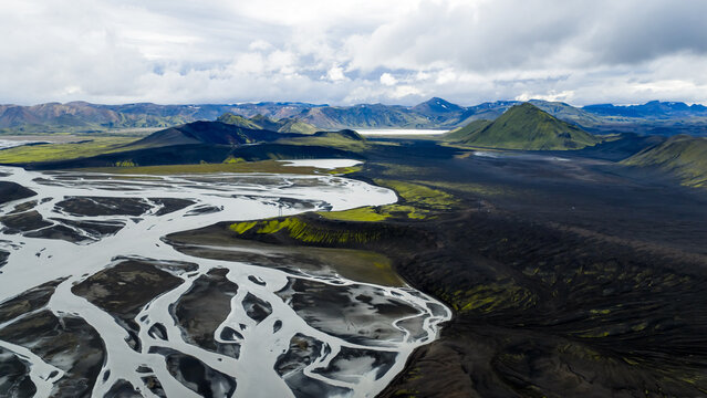 Aerial view of the braided river system winding through the volcanic landscape of Landmannalaugar with mossy green hills and black lava fields in Hella, Rangarthing ytra, Iceland.