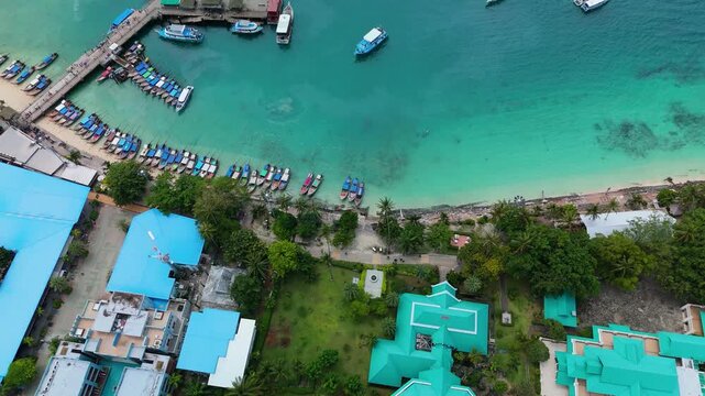 Aerial view of Phi Phi Islands harbor with numerous long-tail boats docked along the pier in the turquoise waters of Mueang Krabi District, Krabi, Thailand.