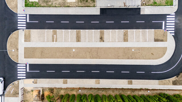 Aerial view of a newly constructed parking lot with white painted parking spaces, asphalt roads, and pedestrian crossings, bordered by a row of green trees in Pancevo, Vojvodina, Serbia.