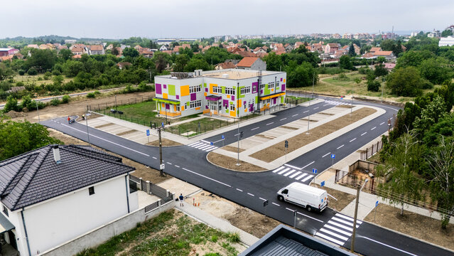Aerial view of a modern school building with colorful facade panels, surrounded by a newly paved parking lot and road infrastructure in Pancevo, Vojvodina, Serbia.