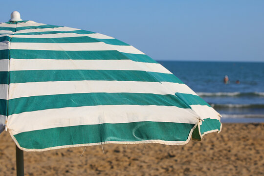 Green and white striped beach umbrella on a sunny seaside shore