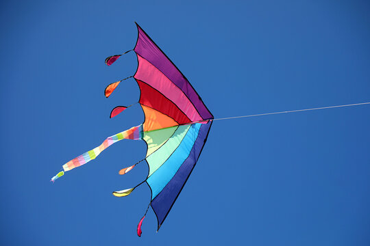 Bright rainbow colored kite flying high in the clear blue sky on a sunny day