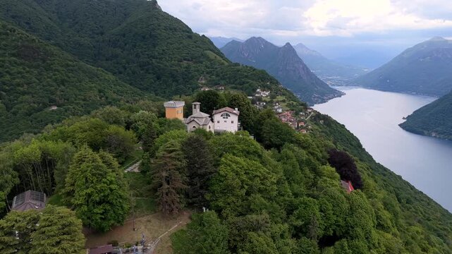 Aerial view of Monte Bre and the historic church atop the mountain, surrounded by lush green forests and the expansive Lake Lugano in Lugano, Ticino, Switzerland.