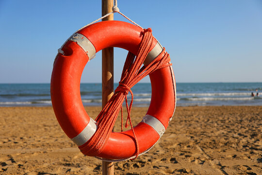 Red lifebuoy hanging on a wooden post at a sandy beach with sea background