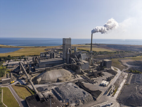 Aerial view of the cement plant with industrial structures, a smoking chimney, and surrounding coastal landscape in Dunbar, Scotland, United Kingdom.