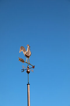 Copper rooster weather vane pointing wind direction against clear blue sky