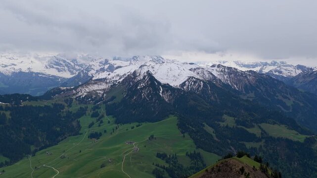 Aerial view of the Stanserhorn mountain landscape featuring snow-capped peaks, lush green alpine meadows, and winding roads in Stans, Nidwalden, Switzerland.