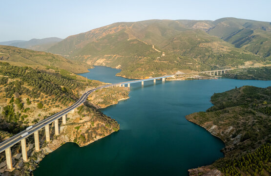Aerial view of the highway bridge spanning the Rules Reservoir surrounded by rolling hills and olive groves in Velez de Benaudalla, Andalusia, Spain.