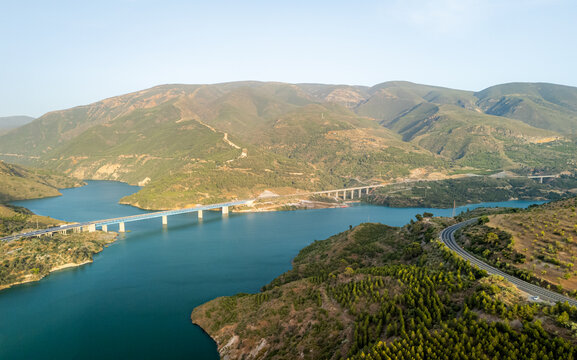 Aerial view of a bridge spanning a turquoise reservoir surrounded by rolling hills and lush greenery in Velez de Benaudalla, Andalusia, Spain.