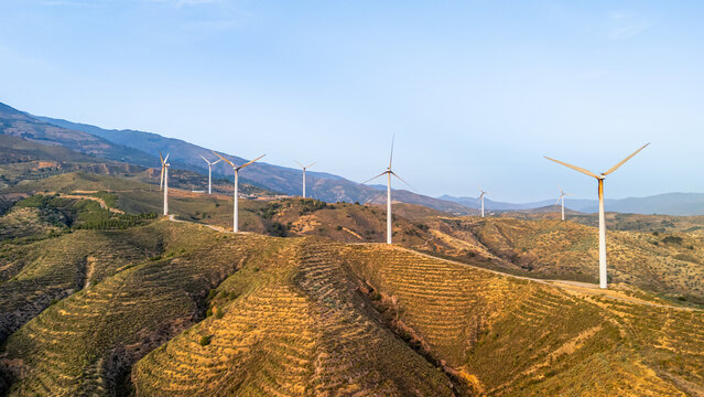 Aerial view of wind turbines situated on rolling hills with dry vegetation under a clear blue sky in Velez de Benaudalla, Andalusia, Spain.
